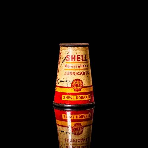 Rare and unique vintage conical shell oil can from 1900–1950 with a red base and yellow accents, featuring the classic shell logo. This antique, cone-shaped motor oil tin is showcased in a studio setting against a solid black background."