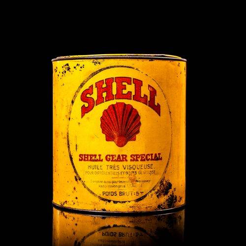 Rare and unique vintage Shell grease can from 1900–1950 with a red base and yellow detailing, featuring the classic Shell logo. This antique lubricant tin is displayed in a studio setting against a solid black background.