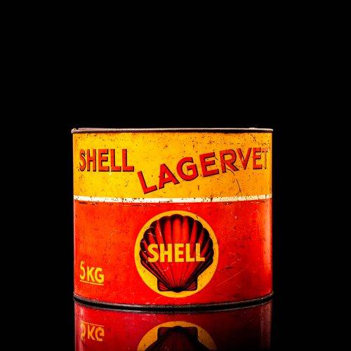 Rare and unique vintage Shell grease can from 1900–1950 with a red base and yellow detailing, featuring the classic Shell logo. This antique lubricant tin is displayed in a studio setting against a solid black background.