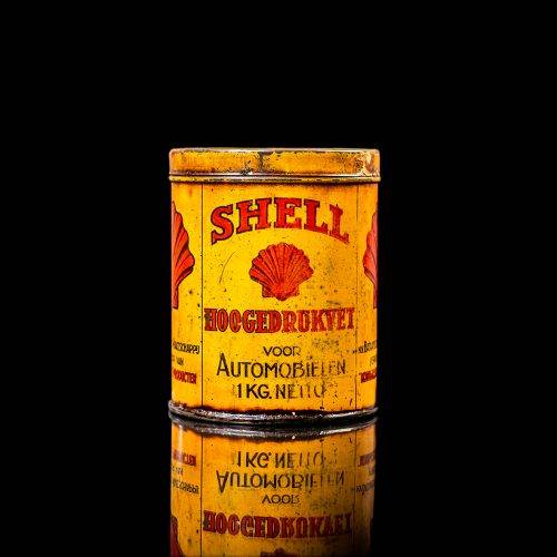 Rare and unique vintage Shell grease can from 1900–1950 with a red base and yellow detailing, featuring the classic Shell logo. This antique lubricant tin is displayed in a studio setting against a solid black background.
