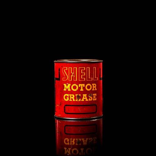 Rare and unique vintage Shell grease can from 1900–1950 with a red base and yellow detailing, featuring the classic Shell logo. This antique lubricant tin is displayed in a studio setting against a solid black background.