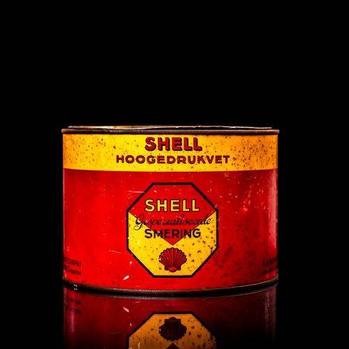 Rare and unique vintage Shell grease can from 1900–1950 with a red base and yellow detailing, featuring the classic Shell logo. This antique lubricant tin is displayed in a studio setting against a solid black background.