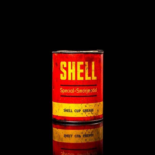 Rare and unique vintage Shell grease can from 1900–1950 with a red base and yellow detailing, featuring the classic Shell logo. This antique lubricant tin is displayed in a studio setting against a solid black background."