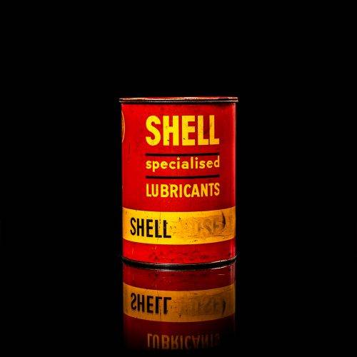 Rare and unique vintage Shell grease can from 1900–1950 with a red base and yellow detailing, featuring the classic Shell logo. This antique lubricant tin is displayed in a studio setting against a solid black background."