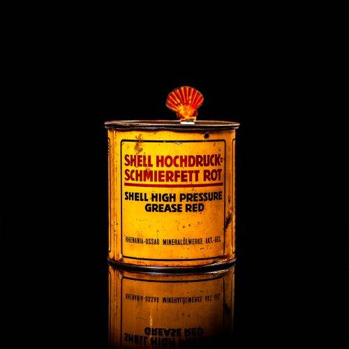 Rare and unique vintage Shell grease can from 1900–1950 with a red base and yellow detailing, featuring the classic Shell logo. This antique lubricant tin is displayed in a studio setting against a solid black background."