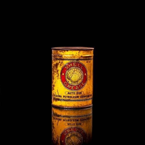 Rare and unique vintage Shell grease can from 1900–1950 with a red base and yellow detailing, featuring the classic Shell logo. This antique lubricant tin is displayed in a studio setting against a solid black background."