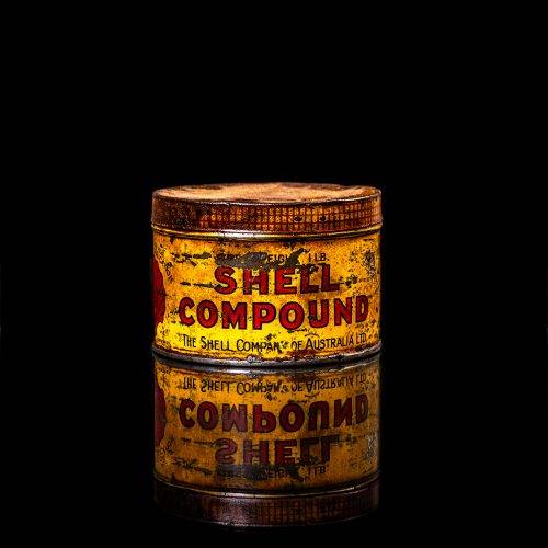 Rare and unique vintage Shell grease can from 1900–1950 with a red base and yellow detailing, featuring the classic Shell logo. This antique lubricant tin is displayed in a studio setting against a solid black background."