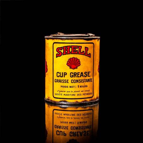 Rare and unique vintage Shell grease can from 1900–1950 with a red base and yellow detailing, featuring the classic Shell logo. This antique lubricant tin is displayed in a studio setting against a solid black background."