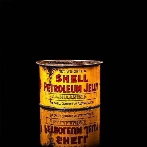 Rare and unique vintage Shell grease can from 1900–1950 with a red base and yellow detailing, featuring the classic Shell logo. This antique lubricant tin is displayed in a studio setting against a solid black background."