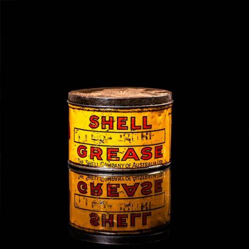 Rare and unique vintage Shell grease can from 1900–1950 with a red base and yellow detailing, featuring the classic Shell logo. This antique lubricant tin is displayed in a studio setting against a solid black background."
