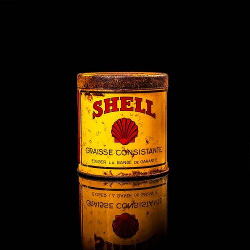 Rare and unique vintage Shell grease can from 1900–1950 with a red base and yellow detailing, featuring the classic Shell logo. This antique lubricant tin is displayed in a studio setting against a solid black background."