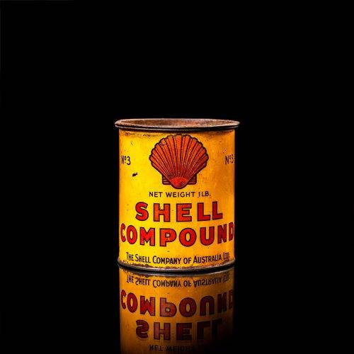 Rare and unique vintage Shell grease can from 1900–1950 with a red base and yellow detailing, featuring the classic Shell logo. This antique lubricant tin is displayed in a studio setting against a solid black background."