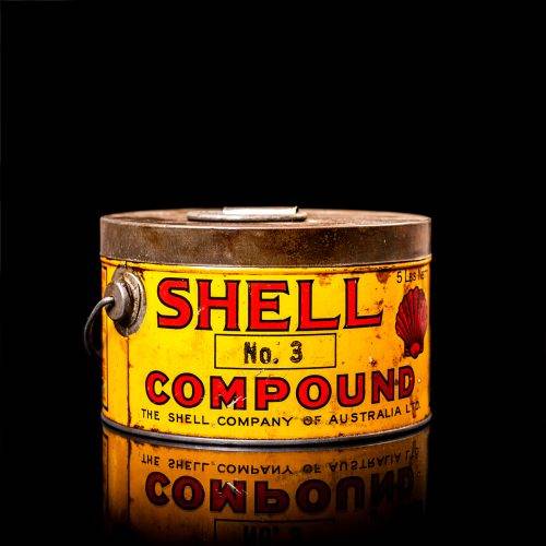 Rare and unique vintage Shell grease can from 1900–1950 with a red base and yellow detailing, featuring the classic Shell logo. This antique lubricant tin is displayed in a studio setting against a solid black background."