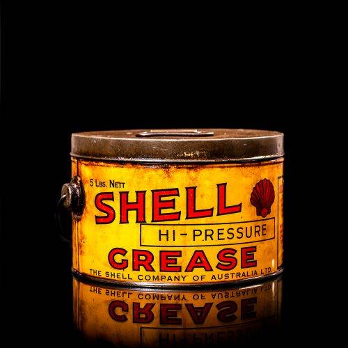 Rare and unique vintage Shell grease can from 1900–1950 with a red base and yellow detailing, featuring the classic Shell logo. This antique lubricant tin is displayed in a studio setting against a solid black background."