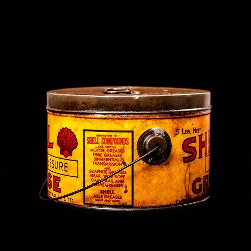 Rare and unique vintage Shell grease can from 1900–1950 with a red base and yellow detailing, featuring the classic Shell logo. This antique lubricant tin is displayed in a studio setting against a solid black background."