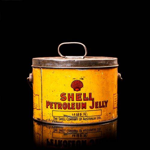 Rare and unique vintage Shell grease can from 1900–1950 with a red base and yellow detailing, featuring the classic Shell logo. This antique lubricant tin is displayed in a studio setting against a solid black background."