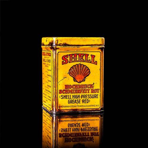 Rare and unique vintage Shell grease can from 1900–1950 with a red base and yellow detailing, featuring the classic Shell logo. This antique lubricant tin is displayed in a studio setting against a solid black background."