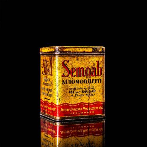 Rare and unique vintage Shell grease can from 1900–1950 with a red base and yellow detailing, featuring the classic Shell logo. This antique lubricant tin is displayed in a studio setting against a solid black background."