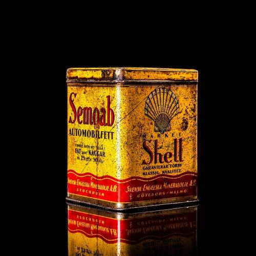 Rare and unique vintage Shell grease can from 1900–1950 with a red base and yellow detailing, featuring the classic Shell logo. This antique lubricant tin is displayed in a studio setting against a solid black background."