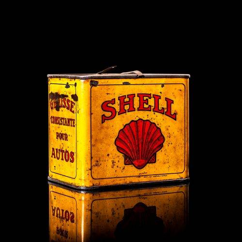 Rare and unique vintage Shell grease can from 1900–1950 with a red base and yellow detailing, featuring the classic Shell logo. This antique lubricant tin is displayed in a studio setting against a solid black background."
