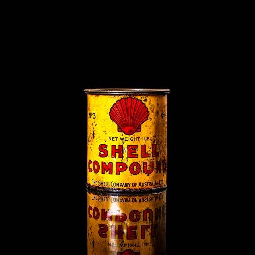 Rare and unique vintage Shell grease can from 1900–1950 with a red base and yellow detailing, featuring the classic Shell logo. This antique lubricant tin is displayed in a studio setting against a solid black background."