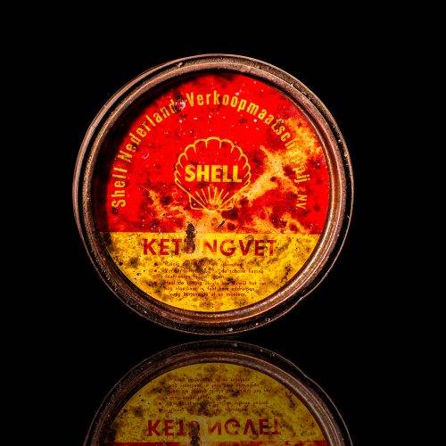Rare and unique vintage Shell grease can from 1900–1950 with a red base and yellow detailing, featuring the classic Shell logo. This antique lubricant tin is displayed in a studio setting against a solid black background."