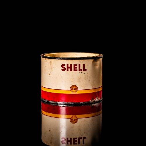 Rare and unique vintage Shell grease can from 1900–1950 with a red base and yellow detailing, featuring the classic Shell logo. This antique lubricant tin is displayed in a studio setting against a solid black background."