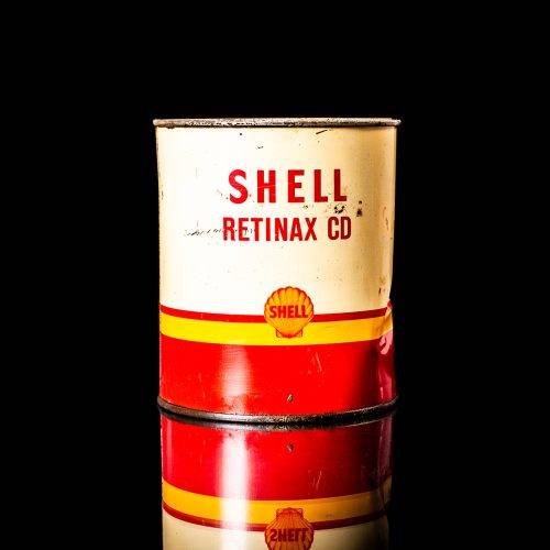 Rare and unique vintage Shell grease can from 1900–1950 with a red base and yellow detailing, featuring the classic Shell logo. This antique lubricant tin is displayed in a studio setting against a solid black background."