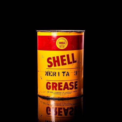Rare and unique vintage Shell grease can from 1900–1950 with a red base and yellow detailing, featuring the classic Shell logo. This antique lubricant tin is displayed in a studio setting against a solid black background."