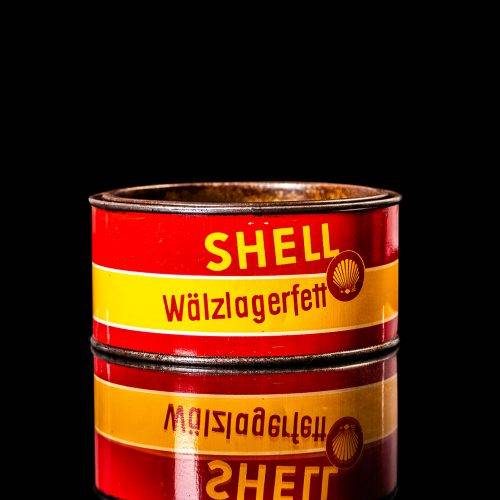 Rare and unique vintage Shell grease can from 1900–1950 with a red base and yellow detailing, featuring the classic Shell logo. This antique lubricant tin is displayed in a studio setting against a solid black background."