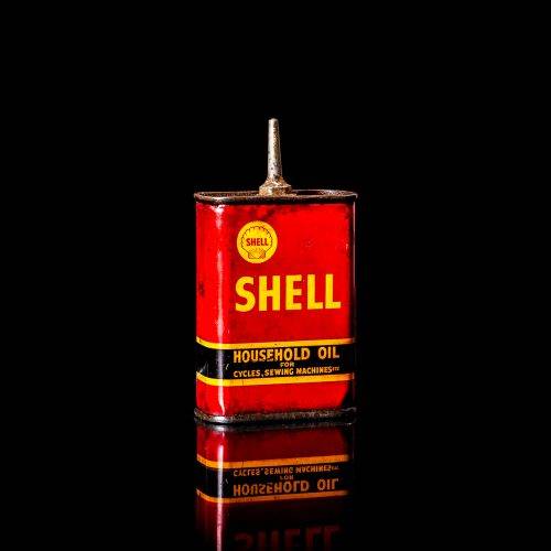 Rare and unique vintage mini Shell oil can Handy oil from 1900–1950 with red and yellow accents, featuring the classic Shell logo. This small antique tin is displayed in a studio setting against a solid black background. Handy oil cans