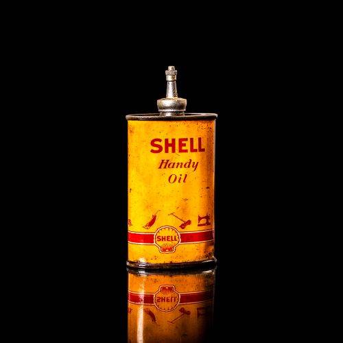 Rare and unique vintage mini Shell oil can Handy oil from 1900–1950 with red and yellow accents, featuring the classic Shell logo. This small antique tin is displayed in a studio setting against a solid black background. Handy oil cans