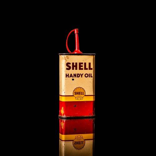 Rare and unique vintage mini Shell oil can Handy oil from 1900–1950 with red and yellow accents, featuring the classic Shell logo. This small antique tin is displayed in a studio setting against a solid black background. Handy oil cans