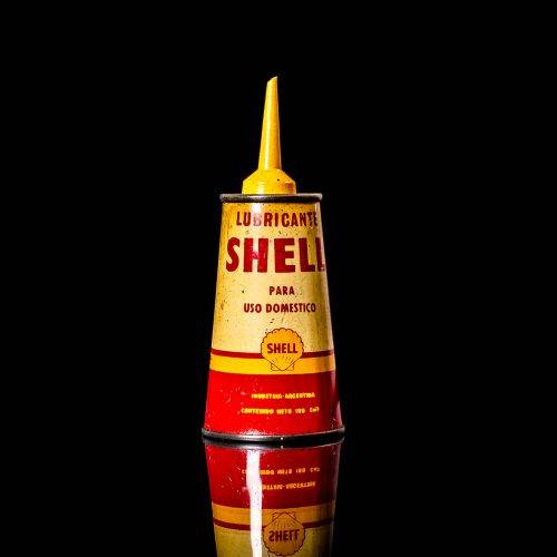 Rare and unique vintage mini Shell oil can from 1900–1950 with red and yellow accents, featuring the classic Shell logo. This small antique tin is displayed in a studio setting against a solid black background. lighter fluid shell cans