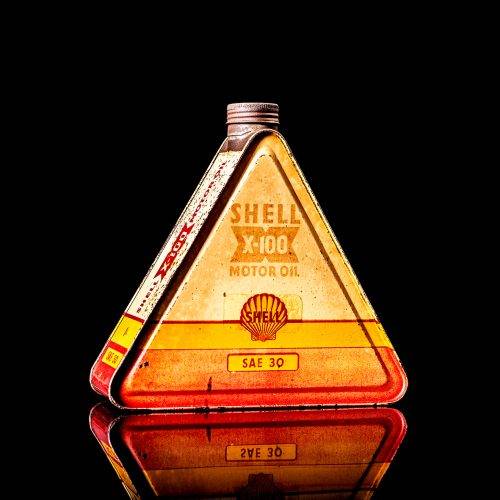 Extremely rare and unique vintage Shell triangular oil can from 1900–1950, featuring red and yellow accents and the classic Shell logo, including a rare shell branding. This antique three-sided tin is displayed in a studio setting against a solid black background.